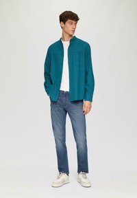 Teal button-up shirt met lange mouwen en een borstzak, gecombineerd met blauwe jeans en witte sneakers. Minimale textuur, casual pasvorm.