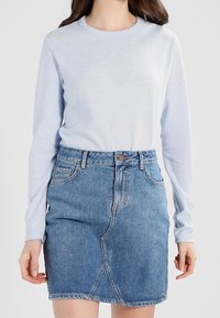 Chemise à manches longues bleu clair associée à une jupe en denim taille haute avec une fente à l'avant et un design classique à cinq poches.