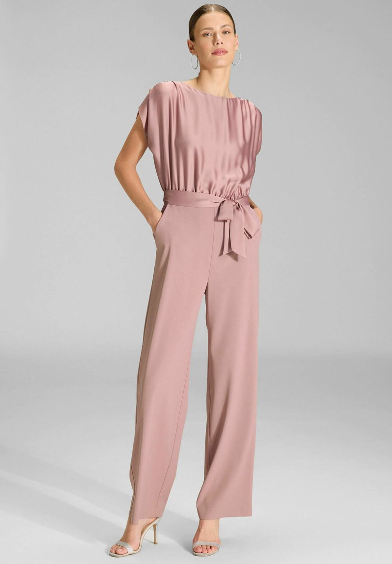 Femme portant un chemisier en satin rose poussiéreux et un pantalon large taille haute assorti avec une ceinture nouée, associé à des sandales à talons beiges.