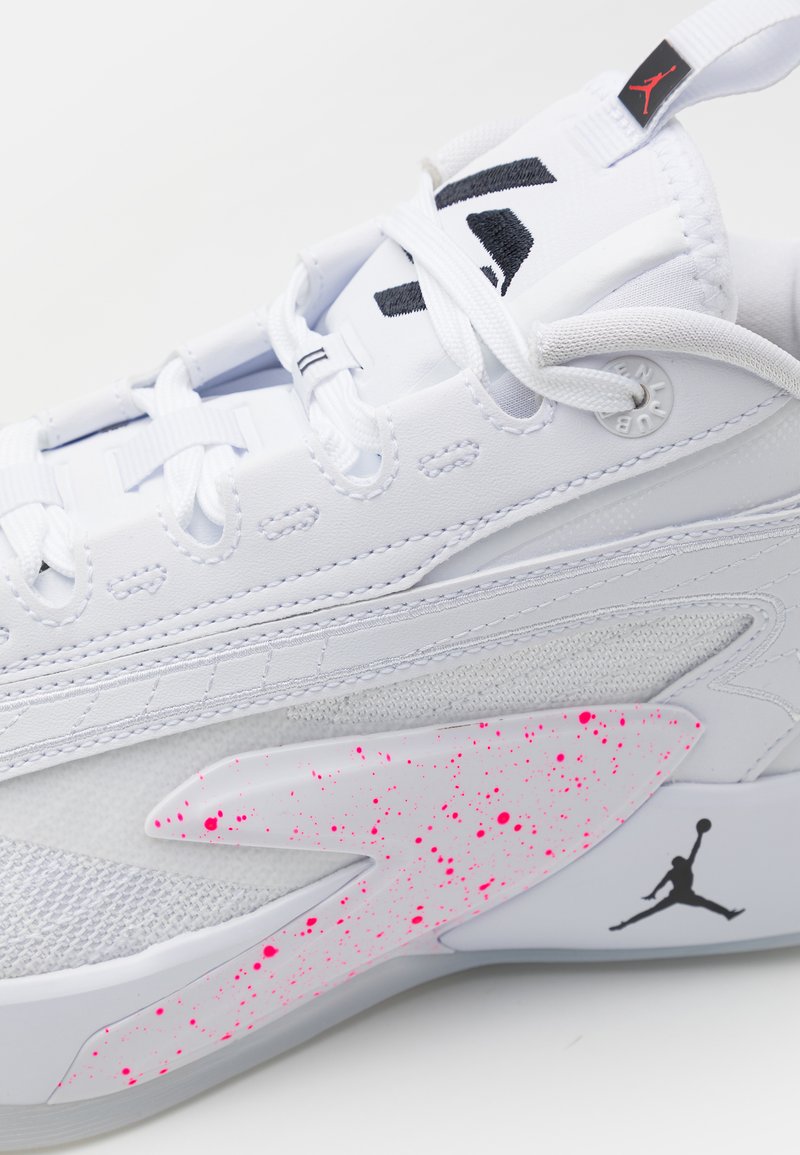 Weißer Sportschuh mit strukturiertem Design, ausgestattet mit pinken Spritzakzenten und einem auffälligen schwarzen Logo. Enthält weiße Schnürsenkel und Nähdetails.