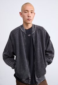 Casaco bomber cinza escuro com fecho de correr à frente, colarinho canelado e bolsos laterais. Apresenta um tecido texturizado e detalhes de costura em contraste.