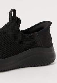 Fekete slip-on sportcipő texturált hálós felsőrésszel, varrás nélküli dizájnnal és tartós gumitalppal, hullámmintával a tapadásért.