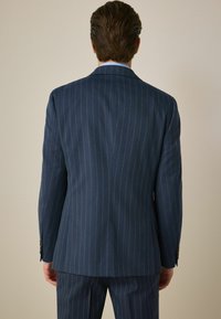 Veste de costume bleu marine à rayures avec une fente unique, des épaules structurées et des accents de boutons. Tissu lisse avec un éclat subtil.