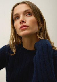 Pull en maille bleu marine avec une texture côtelée et un col rond, featuring des manches longues qui tombent doucement sur les épaules.