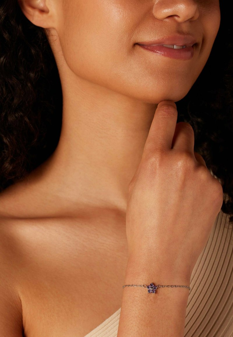 Zilveren armband met een bloemenontwerp en paarse accenten, gedragen om een pols, tegen een achtergrond van neutraal getinte huid.