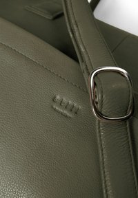 Tume roheline nahast kott tekstureeritud pinnaga. Omab hõbedast metallist pandlat ja reljeefset logot. Puhtad jooned ja lihtne disain.