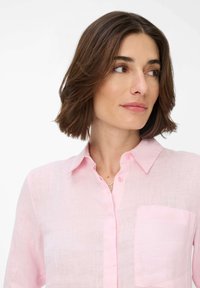 Light pink linen shirt with a button-down collar, a chest pocket, and subtle texture. Features matching buttons and a relaxed fit.
