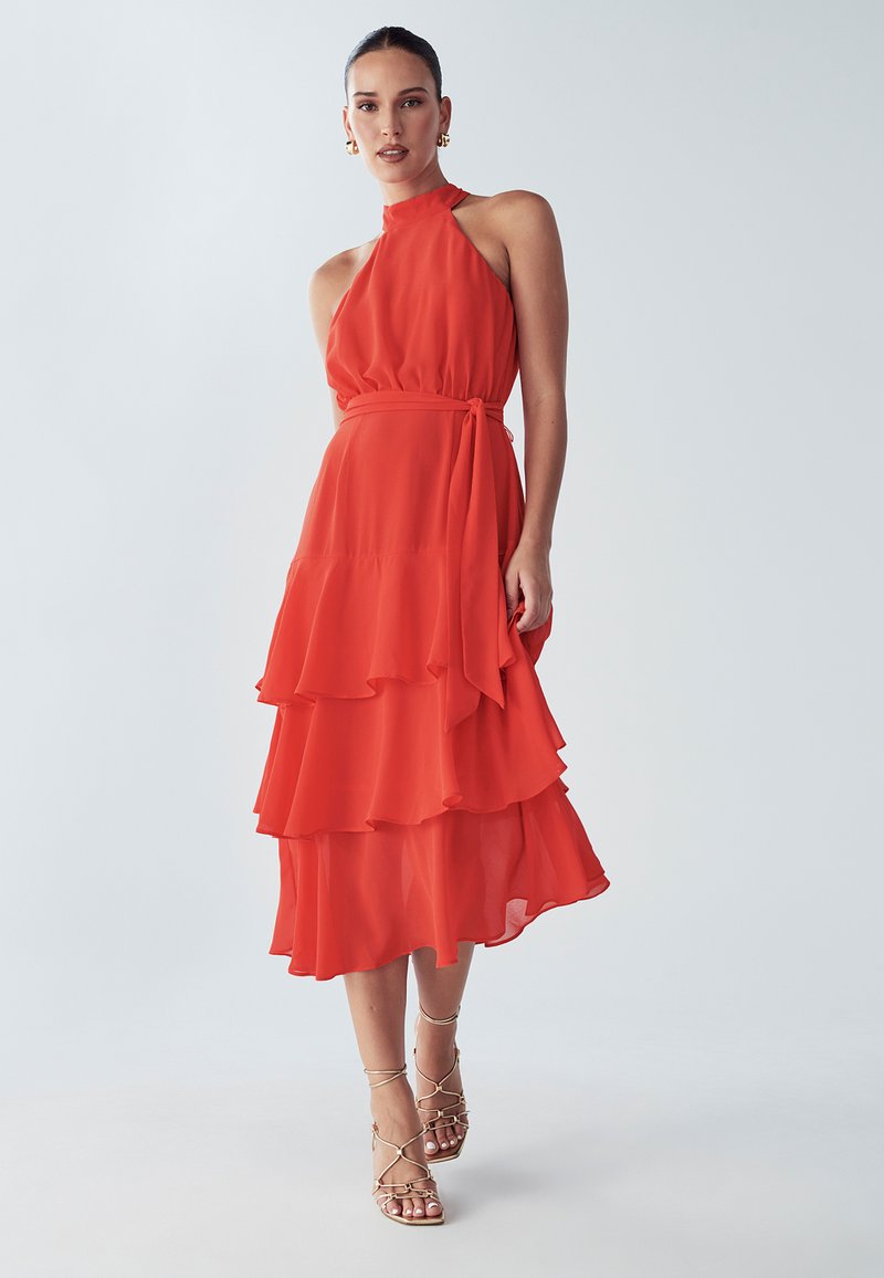 Red, tiered dress made of lightweight fabric with a halter neck and a tied waist. Features ruffled layers and a flowing silhouette.