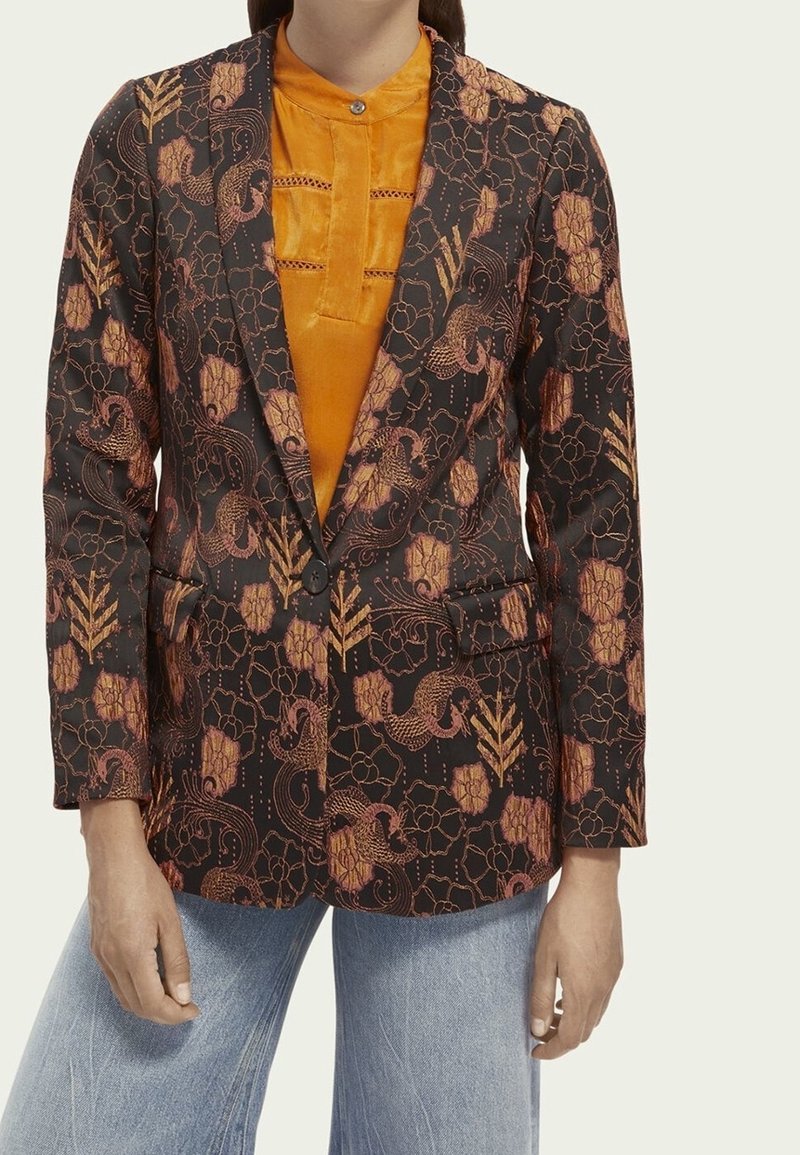 Marynarka z czarnego materiału z pomarańczowymi wzorami kwiatowymi i winorośli, o dopasowanym kroju, z wyłogami i dwiema przednimi kieszeniami. Nałożona na pomarańczowy top.