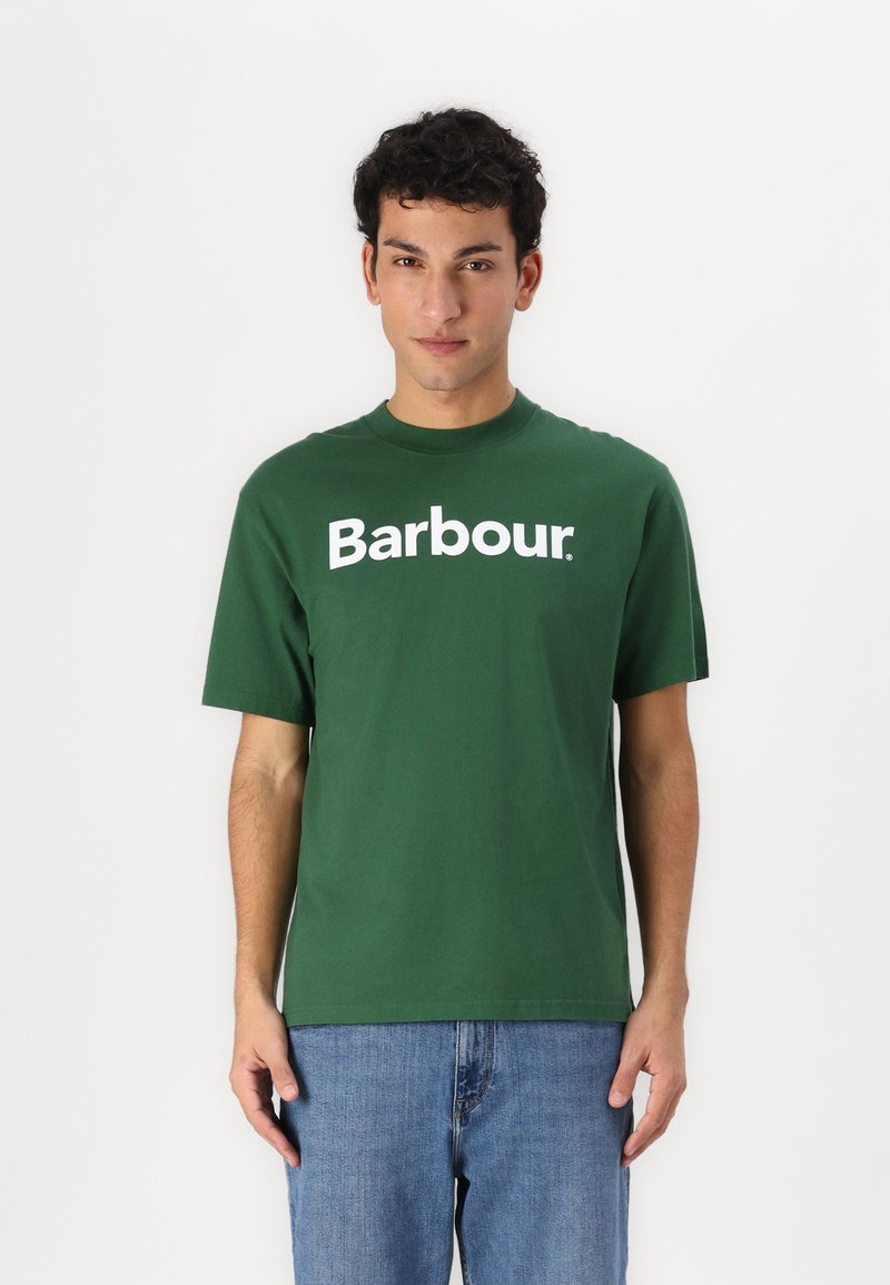 Πράσινο βαμβακερό T-shirt με λευκό λογότυπ�ο "Barbour" μπροστά, κοντά μανίκια και κλασικό στρογγυλό λαιμό, σε συνδυασμό με μπλε τζιν.