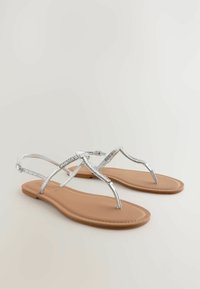Sandali flat argento con finitura lucida, caratterizzati da un design di cinturino elegante e un sottopiede beige. Fibbia regolabile per una vestibilità sicura.