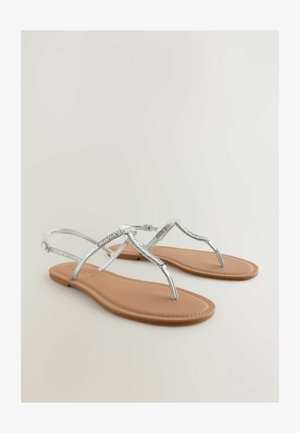 Sandalias planas plateadas con un acabado brillante, que presentan un diseño de tiras elegante y una plantilla beige. Hebilla ajustable para un ajuste seguro.