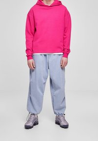 Felpa rosa con cappuccio, jeans azzurri larghi e sneakers grigie con dettagli testurizzati. Vista a corpo intero.