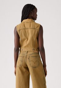 Kafijas krāsas džinsu žakete ar apkakli, bez piedurknēm un divām aizmugurējām kabatām ar izšuvumiem. Aiztaisāma ar metāla pogām.