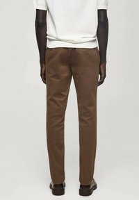 Rjavi hlače iz gladkega blaga, slim fit oblikovanje s ravnimi nogavicami, minimalni šivi in temni, sijoči čevlji.