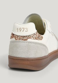 Sneaker bianca con un retro in suede grigio testurizzato; brillante dettaglio in glitter rosé oro; marchio impresso "1973" e "PEPE JEANS" sui lati.