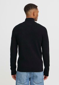 Jersey negro de cuello alto en material de punto suave, con mangas largas y un diseño ajustado, combinado con unos jeans de mezclilla azul claro.