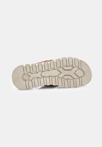 Fehér gumis sneaker talp, mély barázdákkal. A felsőrész egy textúrált, vörösesbarna anyagból készült, amely tapadást és tartósságot biztosít.