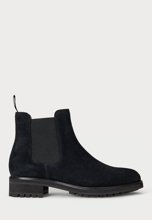 Botines Chelsea de ante negro con paneles laterales de elastano, tirador en el talón y suela de goma gruesa con tacón bajo.