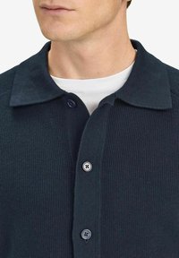 Navy ribbed polo shirt with a buttoned placket, featuring a classic collar and textured fabric. Two buttons visible on the front.