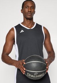 Zwart-witte sporttrui met een V-hals en schouderaccenten, vastgehouden door een persoon, naast een gestructureerde zwarte basketbal met zilveren strepen.