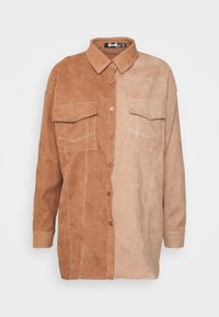 Camisa em blocos de cor castanho e bege, feita de um suave tecido de camurça. Apresenta uma frente com botões, dois bolsos no peito e costuras brancas contrastantes.