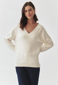 Pulover de culoare crem, dintr-un material moale, cu decolteu în V, margine ribbată și accente de tricot cu model cu sârmă pe mâneci. Purtați-l cu blugi închisi la culoare.