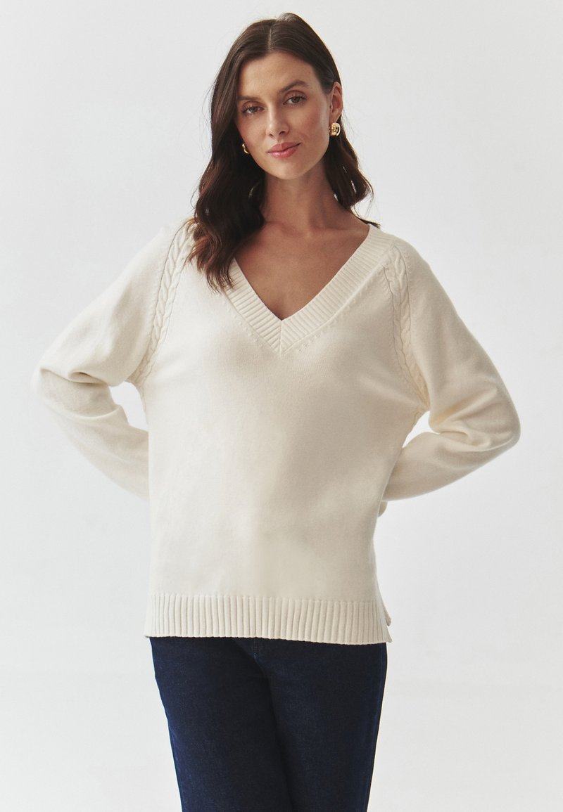 Pulover de culoare crem, dintr-un material moale, cu decolteu în V, margine ribbată și accente de tricot cu model cu sârmă pe mâneci. Purtați-l cu blugi închisi la culoare.