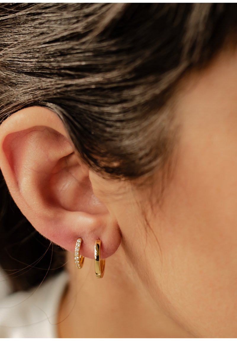 Pendientes de aro de oro con un acabado suave y un pequeño detalle brillante en uno de ellos. Vista en primer plano que resalta la textura y el brillo.