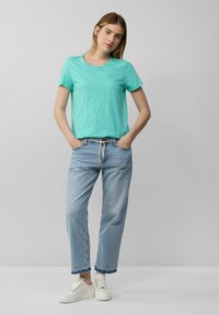 T-shirt en coton turquoise avec un col rond, associé à un jean léger coupe décontractée et des baskets blanches. Tenue simple et décontractée.