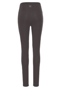 Zwarte leggings met een hoge tailleband, gemaakt van een gladde, rekbare stof en met een klein logo-patch nabij de bovenste achterkant.