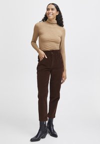 Brown corduroy high-waisted pants with side pockets, paired with a light brown turtleneck top and black ankle boots. Smooth texture.
