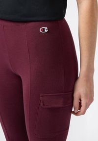 Burgundowe legginsy o dopasowanym kroju, z boczną kieszenią i małym haftowanym logo. Wykonane z miękkiego, elastycznego materiału.