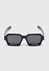 Gafas de sol rectangulares negras con montura gruesa y lentes de tinte oscuro, vistas de frente sobre un fondo claro y liso.