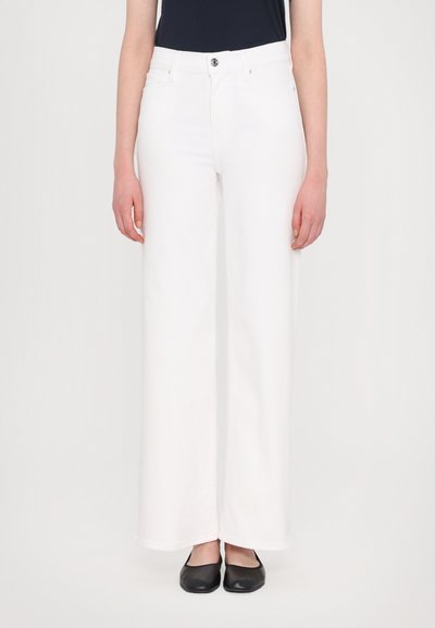 Jeans blancs large avec taille haute, fabriqués en denim, dotés d'une fermeture à bouton à l'avant et de passants de ceinture, associés à des ballerines noires.