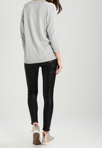 Šedý top s dlouhým rukávem v kombinaci s černými koženými kalhotami a béžovými teniskami. Oblečení má volný střih a hladké textury.