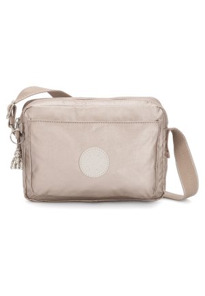 Beige crossbody bag made of smooth fabric. Features a front pocket, a circular logo, and a decorative charm attached to the zipper.
