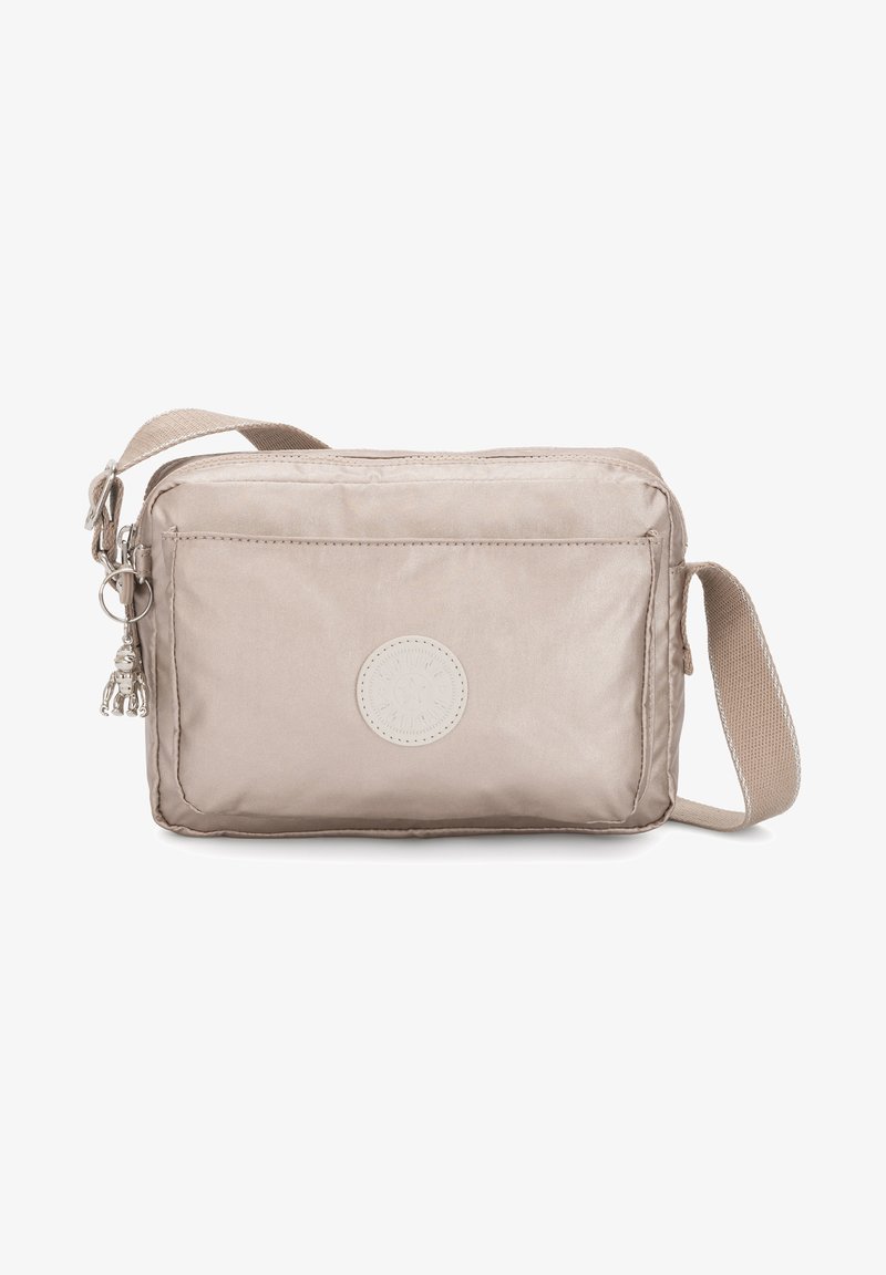 Beige crossbody bag made of smooth fabric. Features a front pocket, a circular logo, and a decorative charm attached to the zipper.