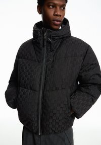 Schwarze Steppjacke mit kariertem Muster, hohem Kragen, Reißverschluss und elastischen Bündchen. Das Material wirkt glatt mit leichtem Glanz.