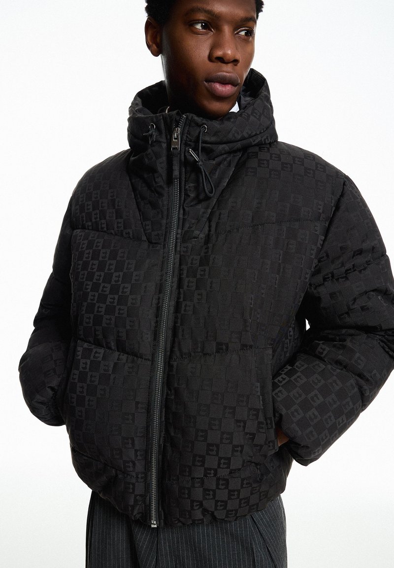 Schwarze Steppjacke mit kariertem Muster, hohem Kragen, Reißverschluss und elastischen Bündchen. Das Material wirkt glatt mit leichtem Glanz.