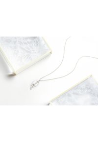 Sølv halskæde med en dråbeformet vedhæng og en blomsteraccent med små krystaller, vist nær to klare, dekoreredeæsker.