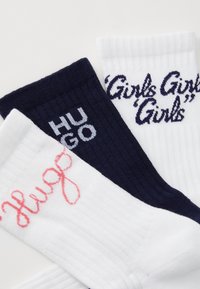 Tre par strumpor: ett par marinblå med "HUGO" i vitt, ett par vita med "Girls Girls Girls" i mörkblått, och ett par vita med "hug" i rosa.