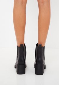 Czarne botki za kostkę wykonane z gładkiej skóry, z blokowym obcasem, elastycznymi bocznymi panelami oraz pętelkami do łatwego zakładania.