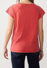 Rød kortærmet t-shirt med rund halsudskæring, der har en subtilt tekstureret stof og en afslappet pasform, båret sammen med mørke jeans.