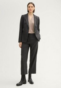 Gray textured suit with a fitted blazer and straight-leg trousers, worn over a light beige top, complemented by black ankle boots.