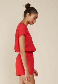 Romper en lin rouge avec des manches courtes, tissu texturé, taille élastique et ourlet festonné. Présente une silhouette décontractée et un design simple.