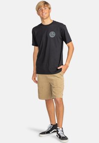Black cotton t-shirt with circular logo on chest, paired with tan corduroy shorts, and black sneakers. Fabric is smooth, casual fit.