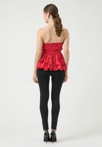 Rød strapless peplum top med rosedetaljer; tekstureret elastisk bånd og volangkant. Sammen med sorte leggings og højhælede sko.