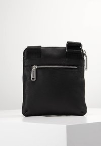 Svart läder crossbody-väska med texturerad yta, dragkedjeförsett framfack och justerbara remmar. Silverfärgade detaljer fulländar designen.