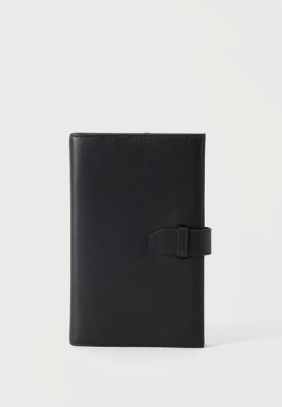 Carnet en cuir noir avec fermeture à sangle centré sur un fond clair uni.